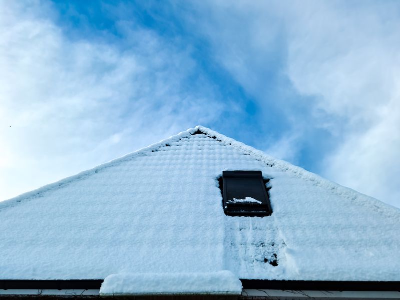 Open roof window in velux style with black roof tiles covered in snow